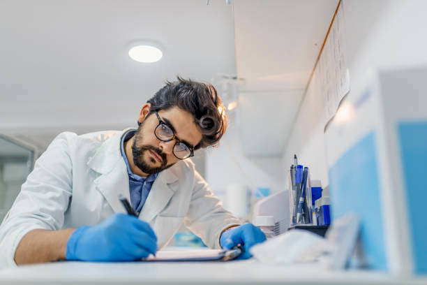 Portrait of a doctor writing a prescription View of male doctor writing in clipboard. Male doctor writing prescription white sitting at desk in hospital. Medicine, profession, technology and people concept - Happy male doctor with clipboard in medical office technology office equipment laboratory stock pictures, royalty-free photos & images