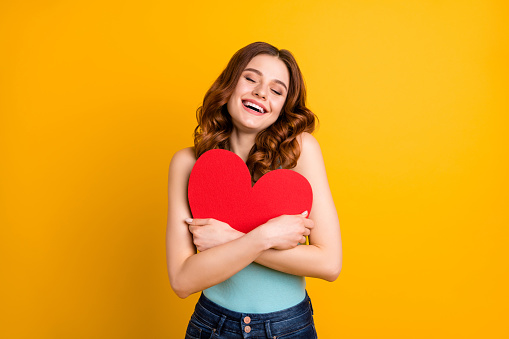 Photo of pretty lady holding big, paper heart close to chest wear tank-top and jeans isolated yellow background