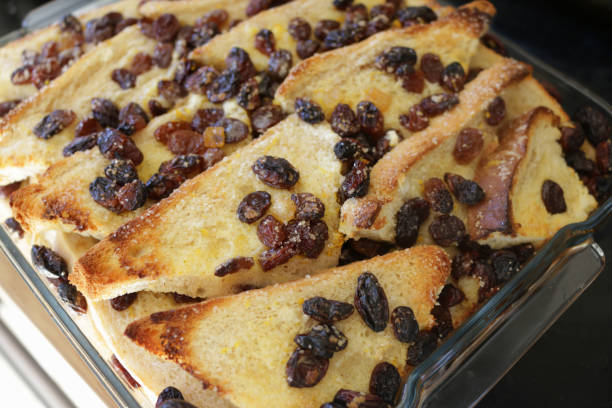 immagine di teglia di vetro contenente ingredienti cotti per un pane stratificato e budino al burro, fette di strati di pane bianco imburrato cosparsi di frutta secca e mele rosse e verdi a dadini - apple and currant bread foto e immagini stock