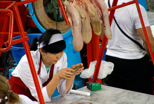 Almaty, Kazakhstan - August 17, 2019: Bored saleswoman playing with her smartphone in the meat section of the Green Bazaar of Almaty, Kazakhstan.