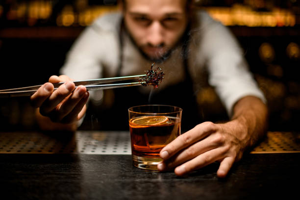male bartender adding chilled brown caramel with twezzers to the cocktail with ice cubes - drink on top of ice food imagens e fotografias de stock