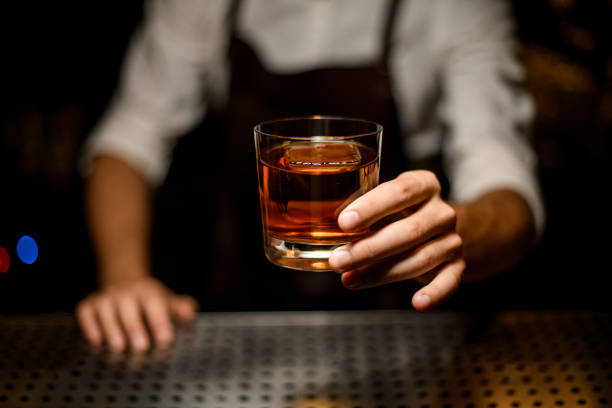 professioneller barkeeper serviert einen cocktail im glas mit einem großen eiswürfel - whisky stock-fotos und bilder