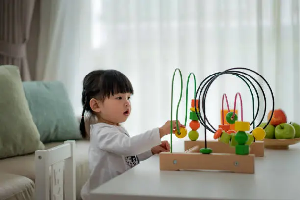 Photo of Adorable Asian Toddler baby girl sitting on chair and playing with color developmental toys at home.