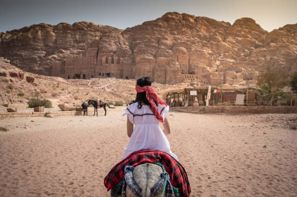 Asian woman tourist riding donkey in Petra, Jordan Asian woman tourist in white dress riding donkey in Petra ancient city of Jordan. Travel UNESCO World Heritage Site in Middle East. donkey animal themes desert landscape stock pictures, royalty-free photos & images