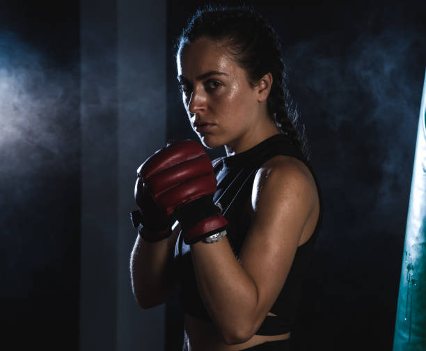 joven boxeadora boxeadora golpeando una bolsa en un entrenamiento deportivo en un gimnasio. - mujer luchadora fotografías e imágenes de stock