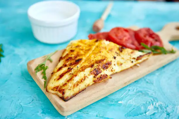 Photo of Grilled pike fillet with tomatoes on wooden board on blue background. Grilled seafood. Barbecue fish. Copy space. Healthy food.
