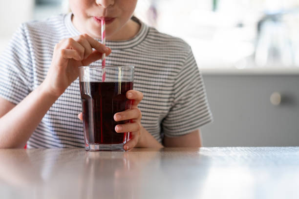 fermez-vous vers le haut de la fille buvant le soude pétillant sucré du verre avec la paille - cold drink photos et images de collection