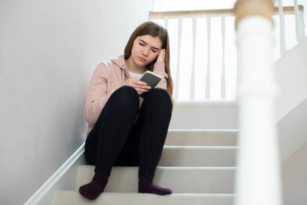 Unhappy Teenage Girl Being Bullied By Text Message Sitting On Stairs At Home Unhappy Teenage Girl Being Bullied By Text Message Sitting On Stairs At Home sad 15 years old girl stock pictures, royalty-free photos & images