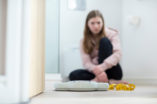 Infeliz adolescente sentada en el baño mirando escalas y cinta métrica photo