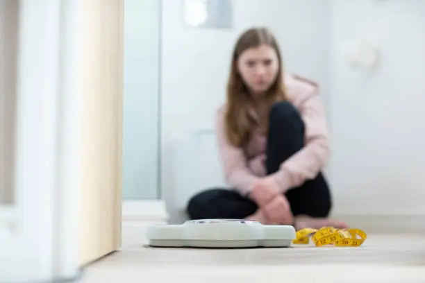 Photo of Unhappy Teenage Girl Sitting In Bathroom Looking At Scales And Tape Measure