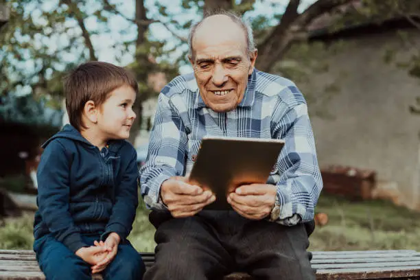 Great grandfather and great grandson together with digital tablet outdoors.