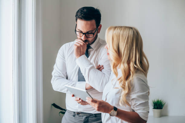 Businessman and businesswoman on a meeting Coworkers standing in the office and looking at digital tablet. worried man standing stock pictures, royalty-free photos & images