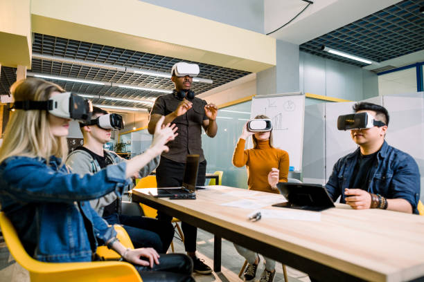 istock Enjoying new experience. Handsome young African man in VR headset gesturing and smiling while standing at the table. Young people wearing vr goggles 1172723676