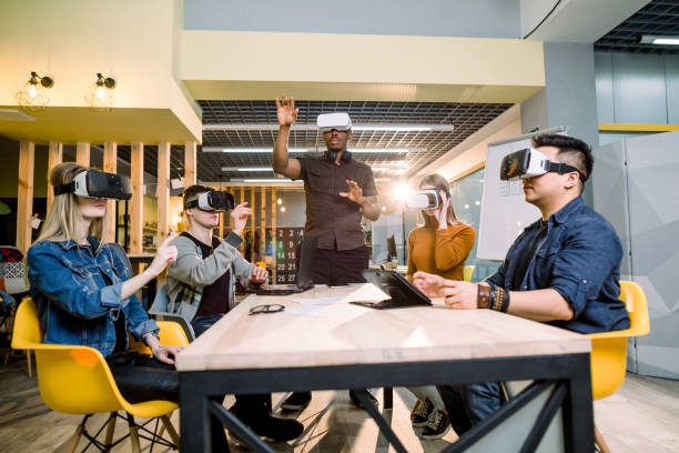 istock Testing games. Young African man wearing virtual reality headset and gesturing while standing at the desk in creative office together with four multiethnical friends 1172723851