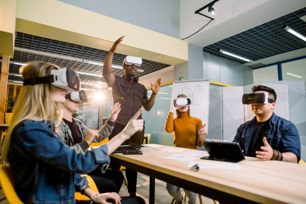 istock Enjoying new experience. Handsome young African man in VR headset gesturing and smiling while standing at the table. Young people wearing vr goggles 1172723858