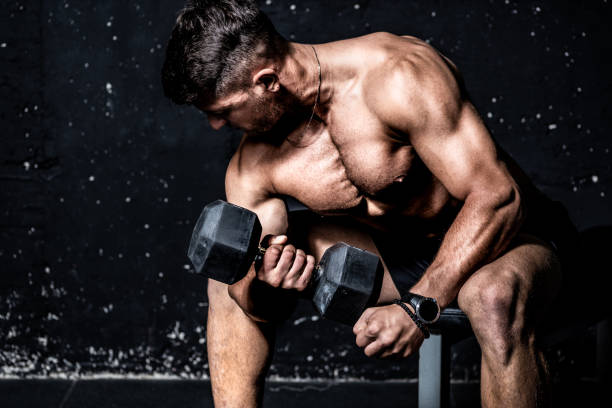 young strong muscular sweaty man biceps muscle workout training with heavy dumbbell in the gym dark image with shadows real people - shirtless energy action effort imagens e fotografias de stock