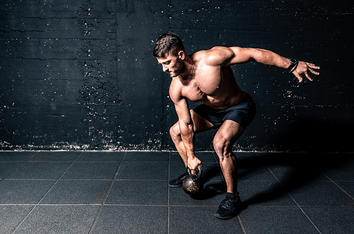 Kettlebell workout, Young strong sweaty focused fit muscular man with big muscles holding heavy kettle bell for training hard core workout in the gym real people
