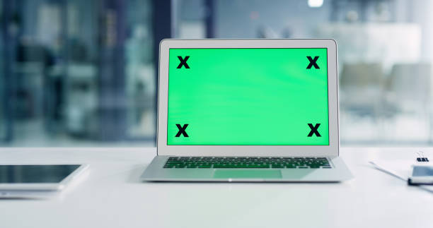 Cropped shot of a laptop with a greenscreen on a desk with other technology pieces in the office