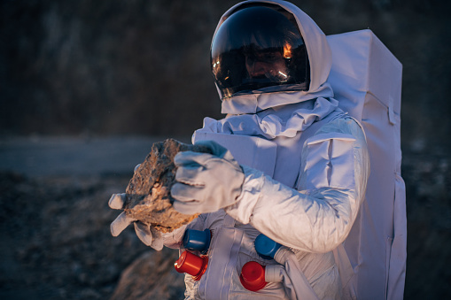 One man, astronaut exploring the land on the other planet alone, holding a rock.