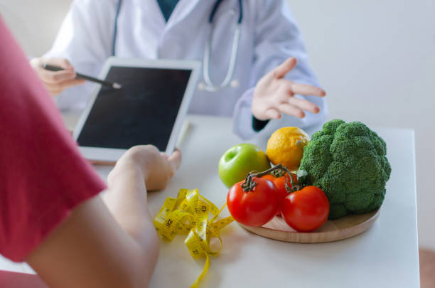 istock friendly nutritionist female doctor using tablet and talking about diet plan with patient and vegetables on desk at laboratory room at office hospital, food science, healthy food and dieting concept 1172733081