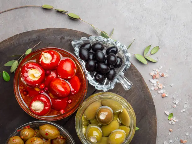 Italian food ingredients Black and green olives in glass bowls and olive oil, stuffed with cheese small bell peppers and red cranberries, herbs, salt Top view on concretebackground with space for text.