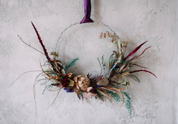 Beautiful hand made everlasting dry wreath made of roses, colourful feathers and eucalyptus on the grey wall background stock photo