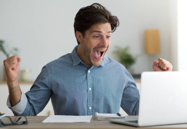 istock Guy Celebrating Success At Laptop Shaking Fists At Workplace 1172739323