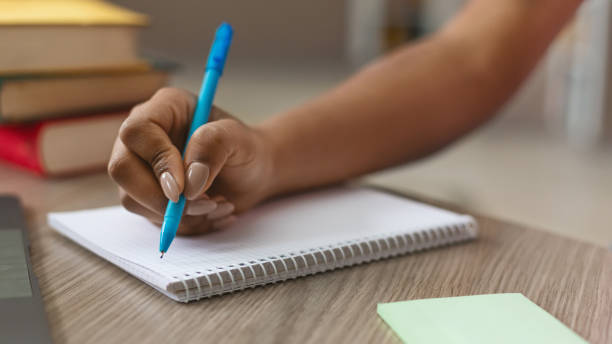 Teen black girl writing notes in notebook African american girl making notes in notebook, sitting at library, cropped exercise book stock pictures, royalty-free photos & images