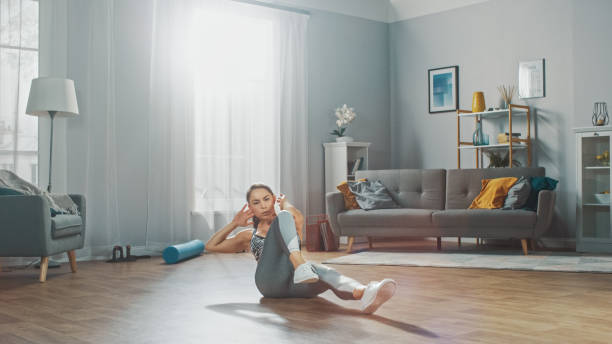 strong and fit beautiful girl in a grey athletic outfit energetically exercising in her bright and spacious living room with minimalistic interior. - beautiful one person strength sensuality imagens e fotografias de stock