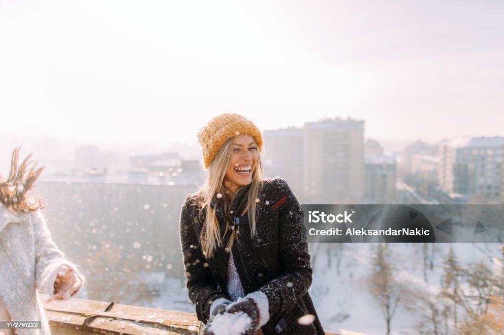 Young woman enjoys snowy winter Young smiling woman enjoys snowy winter day on a rooftop terrace that overlooks the city Winter Stock Photo