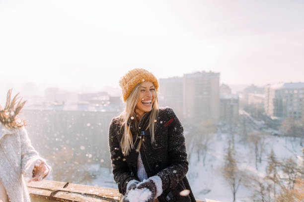 Young woman enjoys snowy winter Young smiling woman enjoys snowy winter day on a rooftop terrace that overlooks the city building terrace photos stock pictures, royalty-free photos & images