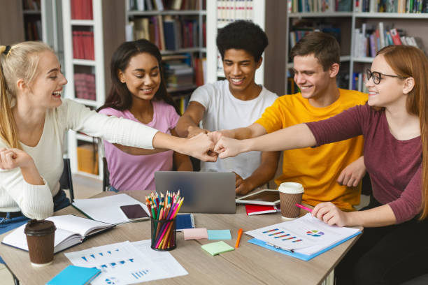 Group of students putting their fists together in library Team work is a way to success. Group of happy students putting their fists together in library, finished preparing their project high school high school student science multi ethnic group stock pictures, royalty-free photos & images