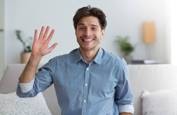 istock Smiling Man Waving Hand Sitting On Sofa Indoor 1172746180