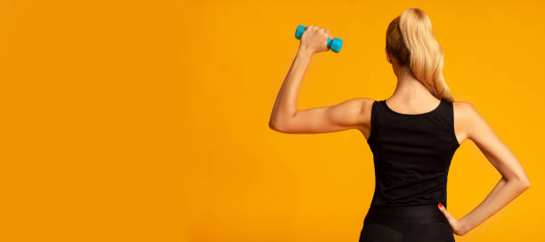 nierozpoznawalna muskularna dziewczyna robi biceps ćwiczenia z hantle w studio - gym yellow muscular build dumbbell zdjęcia i obrazy z banku zdjęć