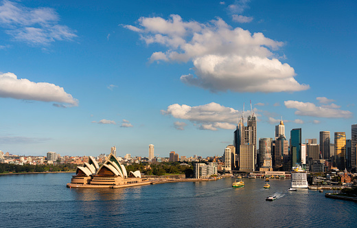 The spectacular cityscape around Sydney Harbour, Australia. The cruise ship Carnival Spirit is moored at the Overseas Terminal next to Circular Quay. Across the water we see the iconic form of the Sydney Opera House and beyond that the Royal Botanic Gardens.