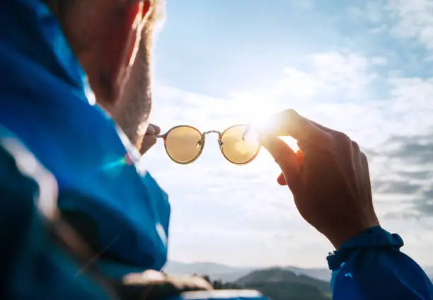 Photo of Backpacker man looking at bright sun through polarized sunglasses  enjoying mountain landscape. Eye & Vision Care human health concept image.