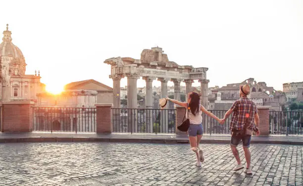 Photo of Young couple tourist walking pointing towards Roman Forum at sunrise. Historical imperial Foro Romano in Rome, Italy from panoramic point of view.