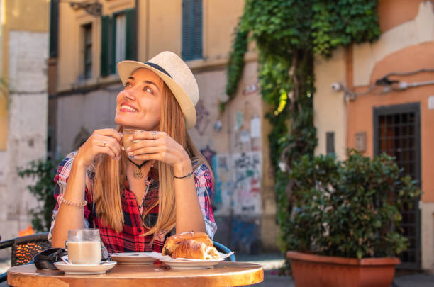 青い目をした若いブロンドの女性は、イタリアのローマの歴史的な近所トラステヴェレの外の典型的なイタリアのバーで朝食を食べています。カプチーノ、コフ、コルネット - italian culture pastry food rome ストックフォトと画像