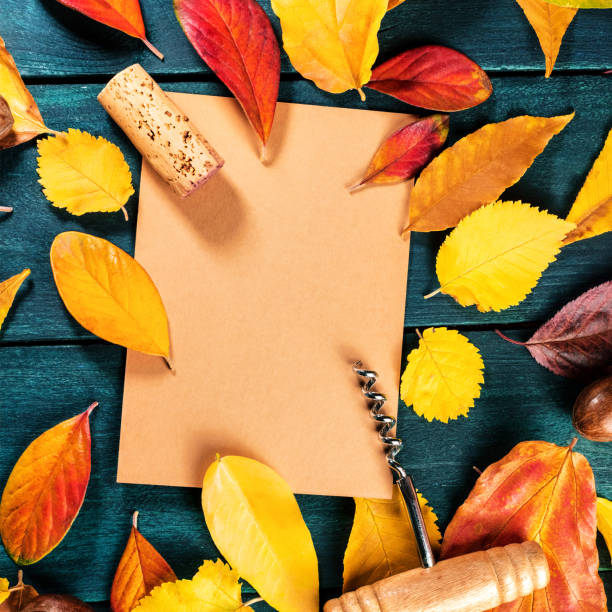 istock Autumn wine design template with a wine cork and corkscrew on a brown kraft paper with vibrant fall leaves forming a frame for text and logo, on a dark rustic wooden background 1172755676
