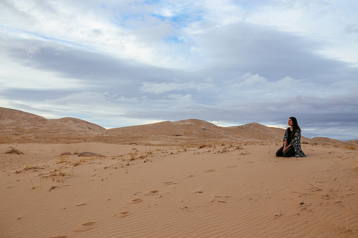 Young hippie woman traveling to the Mojave desert, in between California and Nevada. She is wearing hippie - boho clothing, enjoying the walk through the vast desert landscape, watching the sunset.