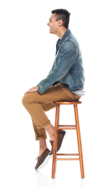 Full length / side view of 20-29 years old adult handsome people / tall person african ethnicity / african-american ethnicity male / young men sitting / resting in front of white background wearing boat shoe / denim jacket who is smiling / happy / cheerful / cool attitude / sitting on stool vista completa / lateral de 20-29 años de edad adulto guapo personas / persona alta etnia africana / etnia afroamericana hombre / hombres jóvenes sentados / descansando frente al fondo blanco usando zapato de barco / chaqueta de mezclilla / actitud fresc