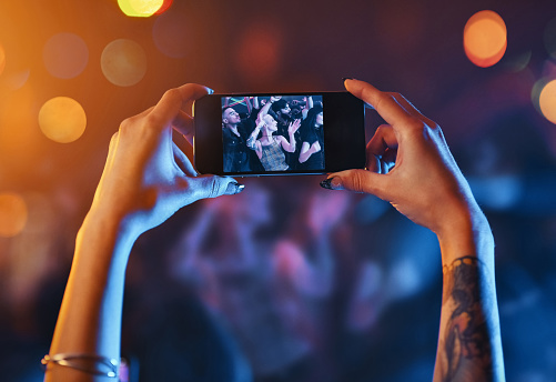 Cropped shot of an unrecognizable young woman holding up a cameraphone while standing at a concert at night