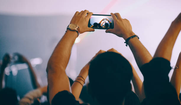 Rearview shot of an unrecognizable young man holding up a cameraphone while standing at a concert at night