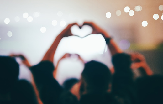 Rearview shot of unrecognizable people making a heart shape while standing at a concert at night
