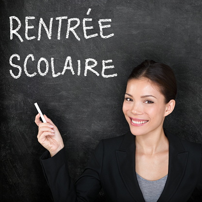 Rentree Scolaire - French teacher woman. Back to School written in French on blackboard by female on chalkboard. Woman professor teaching French language at university, high school or primary school.