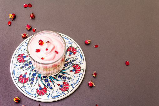 Delicate cream dessert. Traditional turkish edible rose, flower petals. Painted ceramics with a national pattern, stone concrete background, copy space