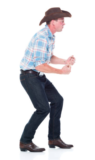 Side view / full length of 20-29 years old caucasian young men / male cowboy standing in front of white background wearing cowboy boot / cowboy hat / hat / lumberjack shirt who is angry / disappointed / frustration / displeased vista lateral / longitud completa de 20-29 años de edad hombres jóvenes caucásicos / vaquero macho de pie frente al fondo blanco con bota de vaquero / sombrero de vaquero / sombrero / camisa de leñador que está enojado / decepcionado / frustración /