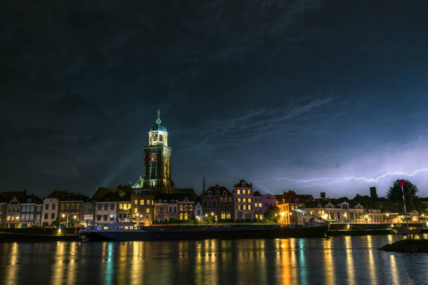 Beautiful night view of the city of Deventer, Holland with colorful reflections in the water of the river Beautiful view of a dutch city along a river at night. Lightning bolt above the skyline of the city. deventer photos stock pictures, royalty-free photos & images