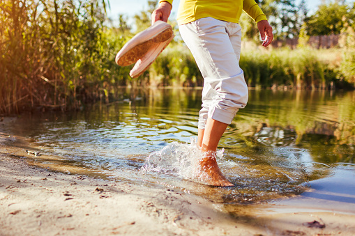 Middle-aged barefooted woman walking on river bank on autumn day. Senior lady having fun in the forest enjoying nature. Closeup of legs