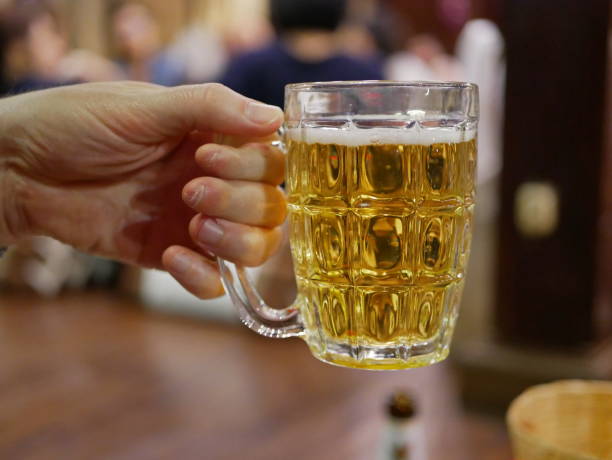 Close up of golden bubbling beer in a cup holding by one hand ready to drink it up with blurry background of people at a party